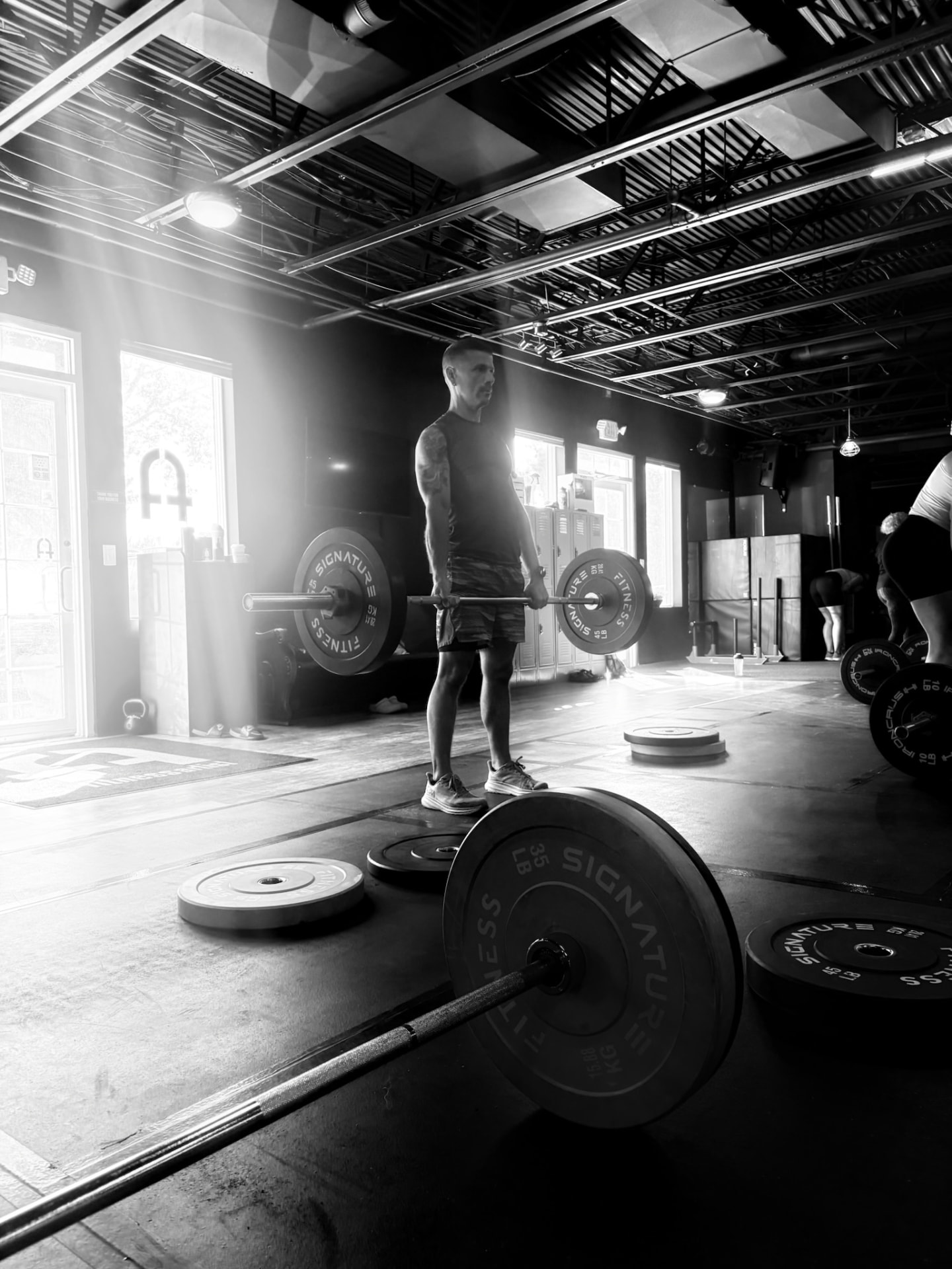 A man holding a loaded barbell at the top of a deadlift inside an industrial training space